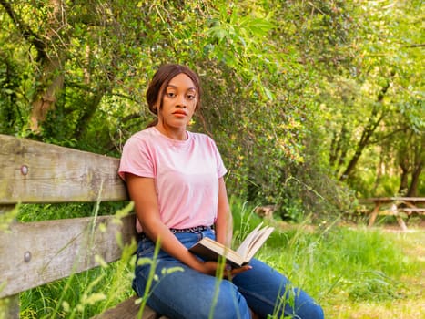 A woman sitting on a bench, engrossed in reading a book.