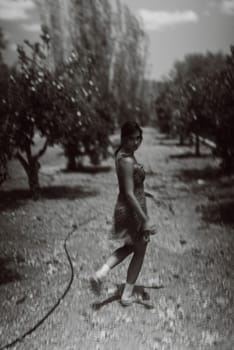 A girl peacefully strolls through a sunlit orchard, reminiscent of a classic, blackandwhite vintage style