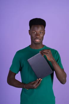 A man wearing a green shirt is standing while holding a laptop in his hands.