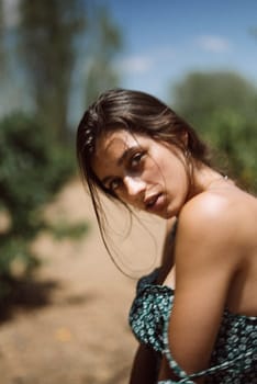 A young woman with an intense gaze is posing outdoors in a stylish summer dress, bathed in natural light