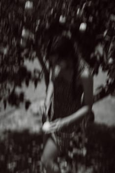 A black and white image of a person picking fruit from a tree in a tranquil environment with a blurred background