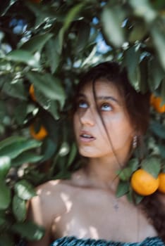 Captivating portrait of a young woman surrounded by lush greenery and vibrant oranges, looking upwards.
