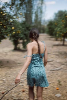 A woman with long, braided hair walks through an orchard on a sunny day, taking in the tranquil countryside scenery