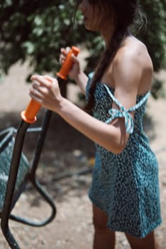 A young woman in a blue dress uses outdoor fitness equipment on a sunny day, enjoying the activity and fresh air