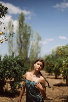 A tranquil scene of a young woman in a green dress standing in an orchard with fruit trees under a clear blue sky