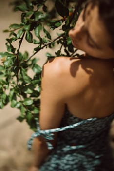 A woman in a floral dress near greenery in sunlight, creating an artistic, dreamy image with a rustic and serene vibe