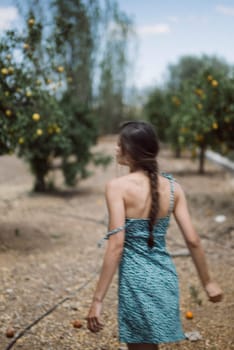 A serene woman in a green dress with a braid is peacefully walking in a fruit tree plantation on a sunny day