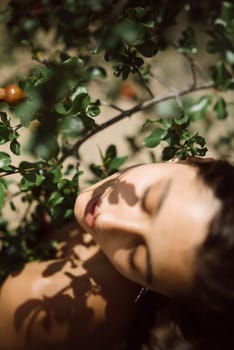 Artistic portrait of a woman lying among greenery and shadows in a soft focus setting, natural beauty.