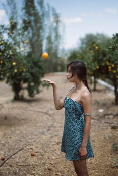 A woman in a summer dress juggles an orange in a lush orchard, embodying joy and carefreeness in nature