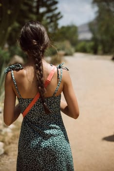 A woman with braided hair walks gracefully on a sandy path outdoors, wearing a summer outfit in soft pastel colors