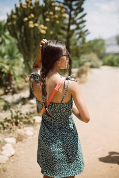 A young woman in a sundress walks outdoors, showcasing nature with trees and plants in the background.