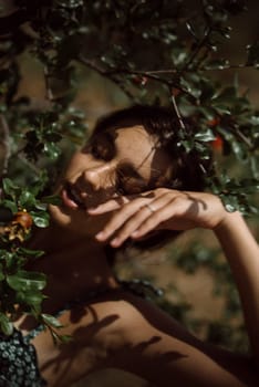 A serene woman standing among green leaves, eyes shut, basking in sunlight and casting soft shadows