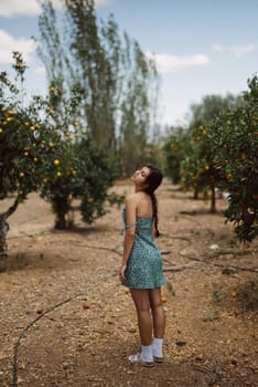 A young woman in a green dress stands in an orange grove, enjoying the peaceful and serene environment.