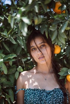 A serene woman poses among orange trees in natural light, exuding calm and peace in a lush grove under the sunlight