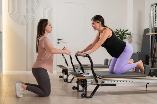 A pregnant woman works out on a reformer exercise machine with a personal trainer