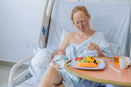 A woman breastfeeds her baby in the hospital while simultaneously having lunch herself. This moment of multitasking illustrates the balance between motherhood and self-care, emphasizing maternal dedication and the nurturing atmosphere of the hospital ward.