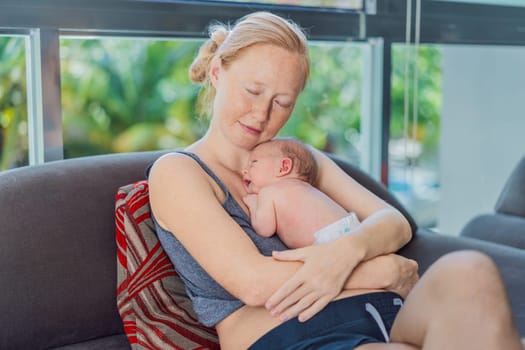 Mom with newborn baby relaxing on the sofa at home. This tender moment highlights the bond between mother and child in a comfortable and loving family environment.