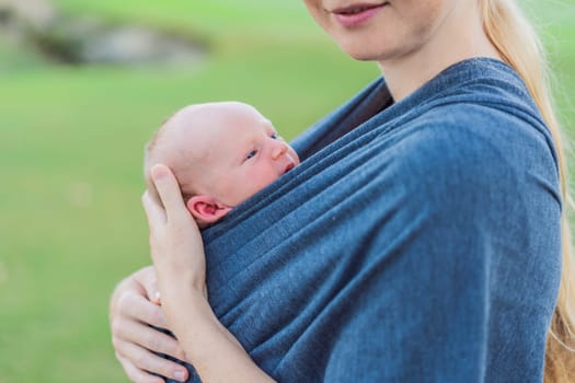 Mom walks with her newborn baby in a sling. This moment highlights the close bond between mother and child, promoting comfort, security, and the benefits of babywearing in everyday life.