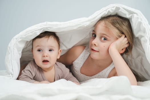 Little girl and her newborn brother hiding under the blanket