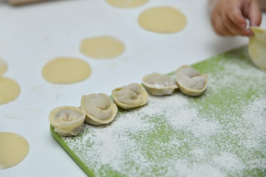 A child's hand making Russian dumplings in a kitchen