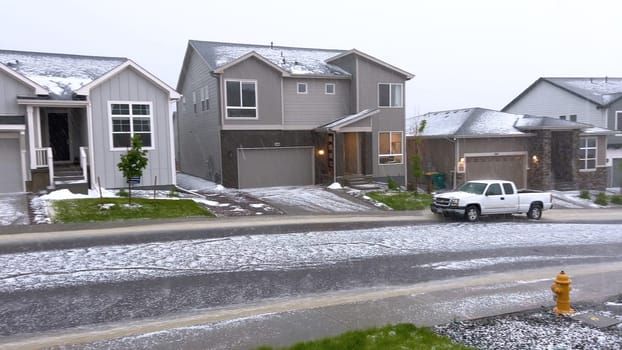 Castle Rock, Colorado, USA-June 12, 2024-Slow motion-A suburban neighborhood with modern houses covered in a layer of hail after a storm. The scene shows a driveway with a car parked, and the street littered with hailstones.