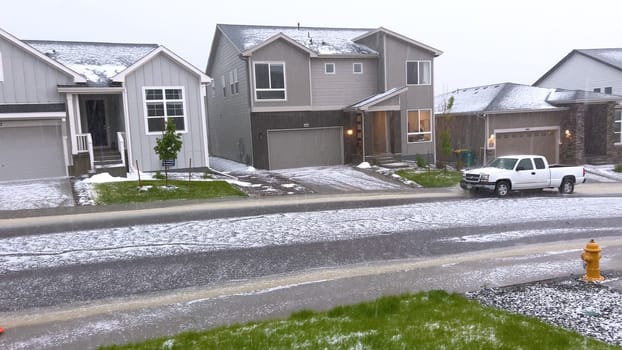 Castle Rock, Colorado, USA-June 12, 2024-Slow motion-A suburban neighborhood with modern houses covered in a layer of hail after a storm. The scene shows a driveway with a car parked, and the street littered with hailstones.