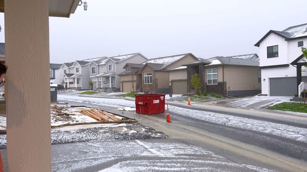 Castle Rock, Colorado, USA-June 12, 2024-Slow motion-A suburban neighborhood with modern houses covered in a layer of hail after a storm. The scene shows a driveway with a car parked, and the street littered with hailstones.