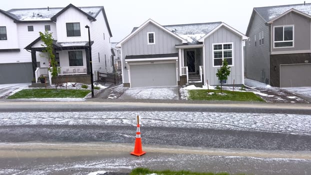 Castle Rock, Colorado, USA-June 12, 2024-Slow motion-A suburban neighborhood with modern houses covered in a layer of hail after a storm. The scene shows a driveway with a car parked, and the street littered with hailstones.