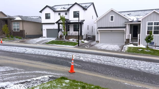 Castle Rock, Colorado, USA-June 12, 2024-Slow motion-A suburban neighborhood with modern houses covered in a layer of hail after a storm. The scene shows a driveway with a car parked, and the street littered with hailstones.