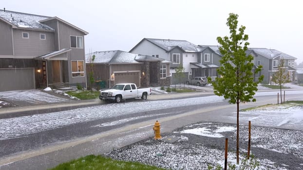 Castle Rock, Colorado, USA-June 12, 2024-Slow motion-A suburban neighborhood with modern houses covered in a layer of hail after a storm. The scene shows a driveway with a car parked, and the street littered with hailstones.