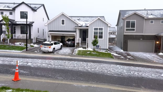 Castle Rock, Colorado, USA-June 12, 2024-Slow motion-A suburban neighborhood with modern houses covered in a layer of hail after a storm. The scene shows a driveway with a car parked, and the street littered with hailstones.