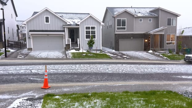 Castle Rock, Colorado, USA-June 12, 2024-Slow motion-A suburban neighborhood with modern houses covered in a layer of hail after a storm. The scene shows a driveway with a car parked, and the street littered with hailstones.