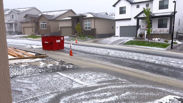 Castle Rock, Colorado, USA-June 12, 2024-Slow motion-A suburban neighborhood with modern houses covered in a layer of hail after a storm. The scene shows a driveway with a car parked, and the street littered with hailstones.