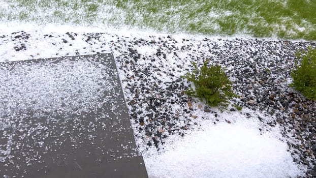 Castle Rock, Colorado, USA-June 12, 2024-Slow motion-A suburban neighborhood with modern houses covered in a layer of hail after a storm. The scene shows a driveway with a car parked, and the street littered with hailstones.