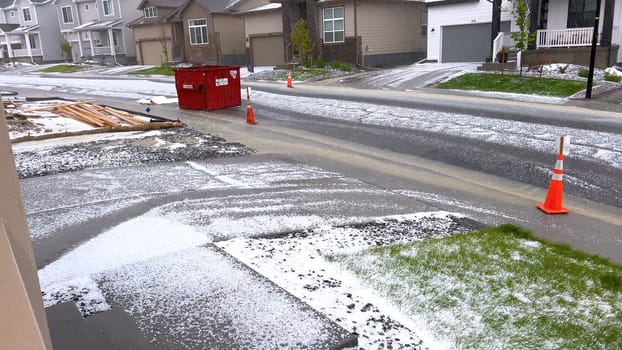 Castle Rock, Colorado, USA-June 12, 2024-Slow motion-A suburban neighborhood with modern houses covered in a layer of hail after a storm. The scene shows a driveway with a car parked, and the street littered with hailstones.