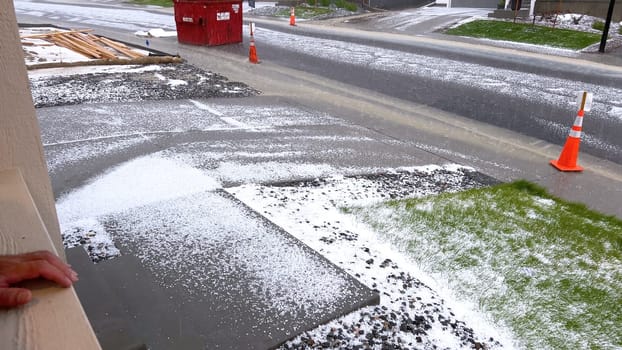 Castle Rock, Colorado, USA-June 12, 2024-Slow motion-A suburban neighborhood with modern houses covered in a layer of hail after a storm. The scene shows a driveway with a car parked, and the street littered with hailstones.