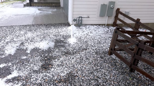 Castle Rock, Colorado, USA-June 12, 2024-Slow motion-A suburban neighborhood with modern houses covered in a layer of hail after a storm. The scene shows a driveway with a car parked, and the street littered with hailstones.