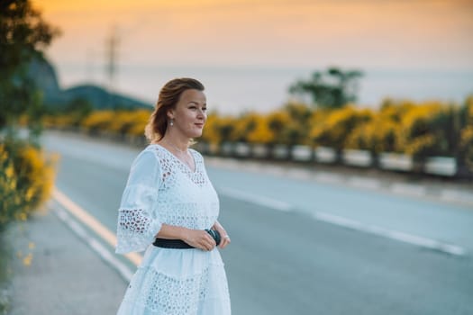 A woman in a white dress stands on a road. The road is empty and the sky is orange