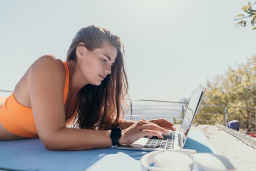 Digital nomad, Business woman working on laptop by the sea. Pretty lady typing on computer by the sea at sunset, makes a business transaction online from a distance. Freelance, remote work on vacation