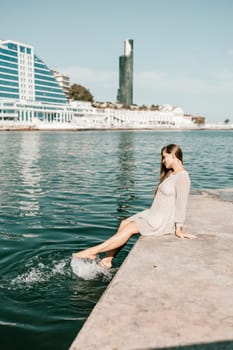 A woman is sitting in the water wearing a white dress. The water is calm and blue. The woman is enjoying the moment and taking in the beauty of the scene