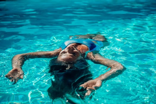 Woman relaxing swimming pool. Happy woman in a blue swimsuit floating in the pool, look form above.