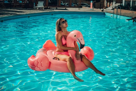 A woman is sitting on a pink inflatable flamingo in a pool. Concept of fun and relaxation, as the woman is enjoying her time in the water