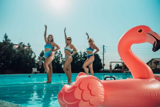 Three women are in the water, one of them is holding a pink flamingo. Scene is fun and playful