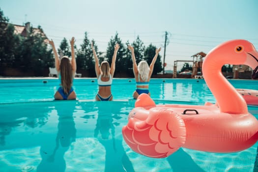 Three women are in a pool with a pink flamingo float. They are all wearing bikinis and are having a good time