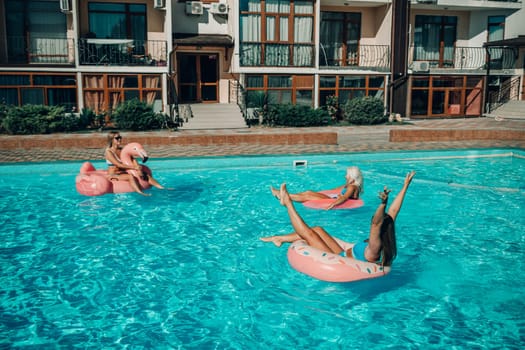 A group of people are in a pool with pink and white floats. Scene is fun and lighthearted