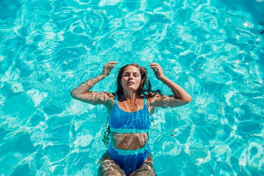 Woman relaxing swimming pool. Happy woman in a blue swimsuit floating in the pool, look form above.