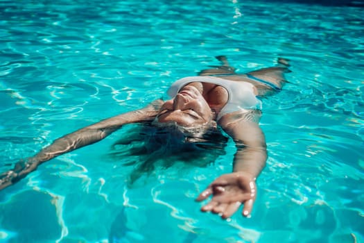 Woman relaxing swimming pool. Happy woman in a blue swimsuit floating in the pool, look form above.