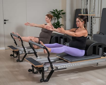 Two pregnant women do Pilates exercises on a reformer. Yoga class for pregnant women