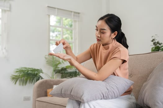 A young woman sitting on a couch at home, taking birth control pills, emphasizing health, wellness, and responsible family planning.