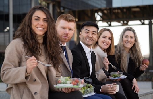 Side view of diverse business people enjoying a lunch break outdoor from office building and looking at camera.